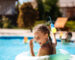 Cheerful children playing waterguns, rejoicing, jumping, swimming in pool. Copy space